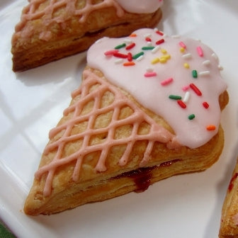 jammy fruit hand pie shaped like an ice cream cone with icing on top on a white plate