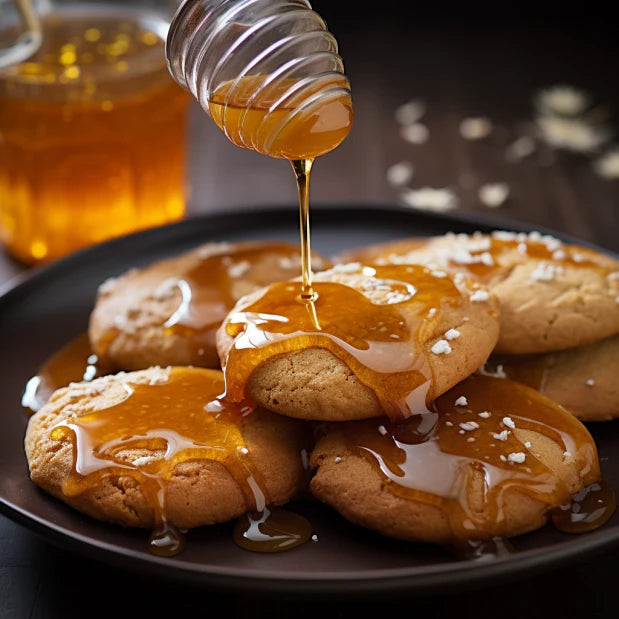 round cookies that are being drizzled with a honey glaze on a black plate with a jar of honey in the background