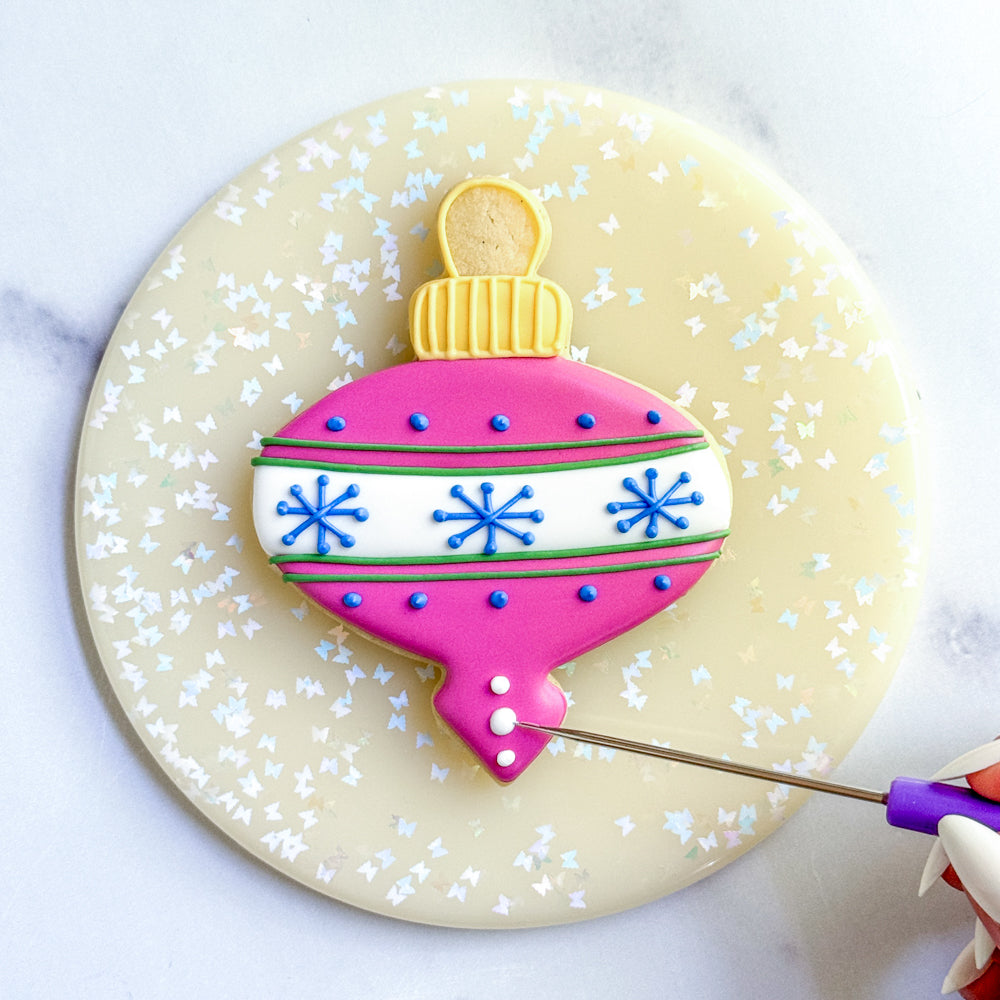 Finial ornament cookie being decorated with fuchsia icing