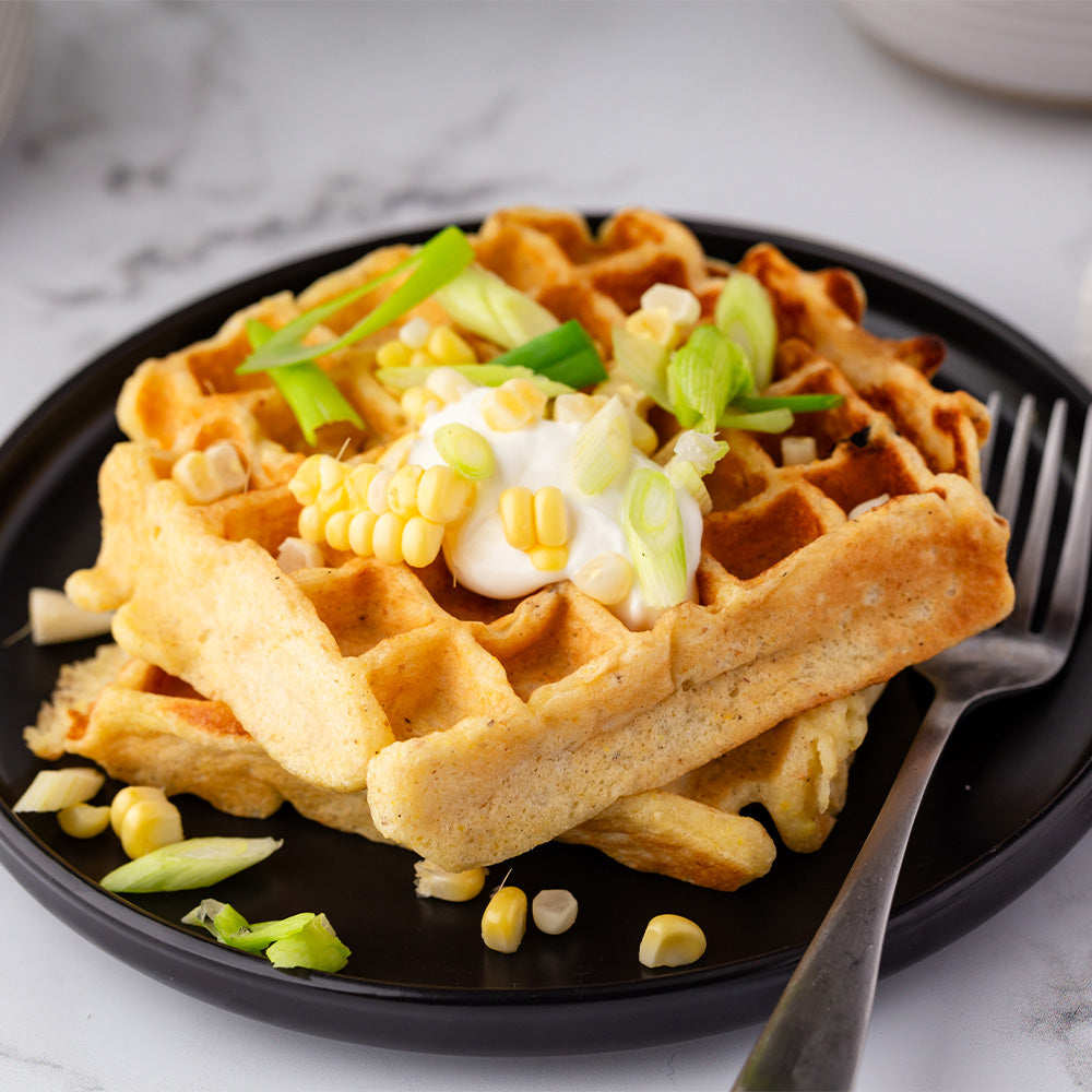 Cornbread waffles topped with sour cream on a black plate