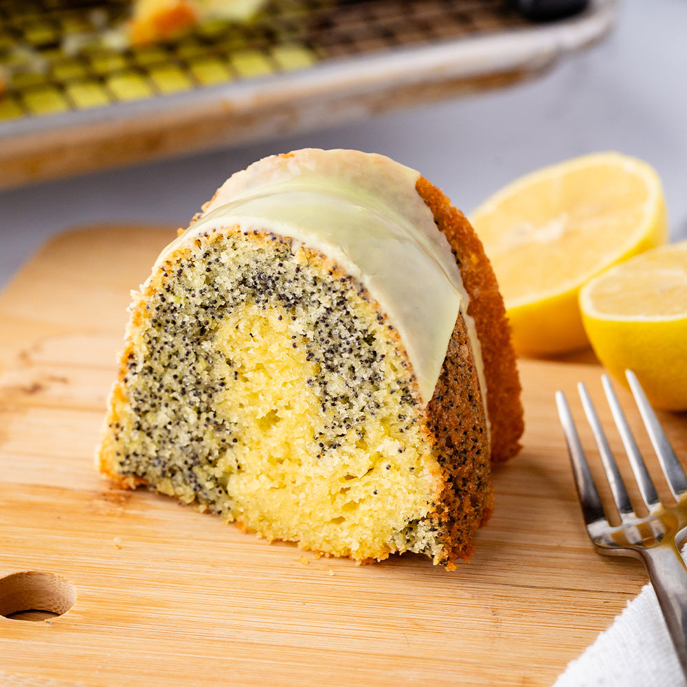 Slice of lemon poppyseed cake with fork and lemons in the background