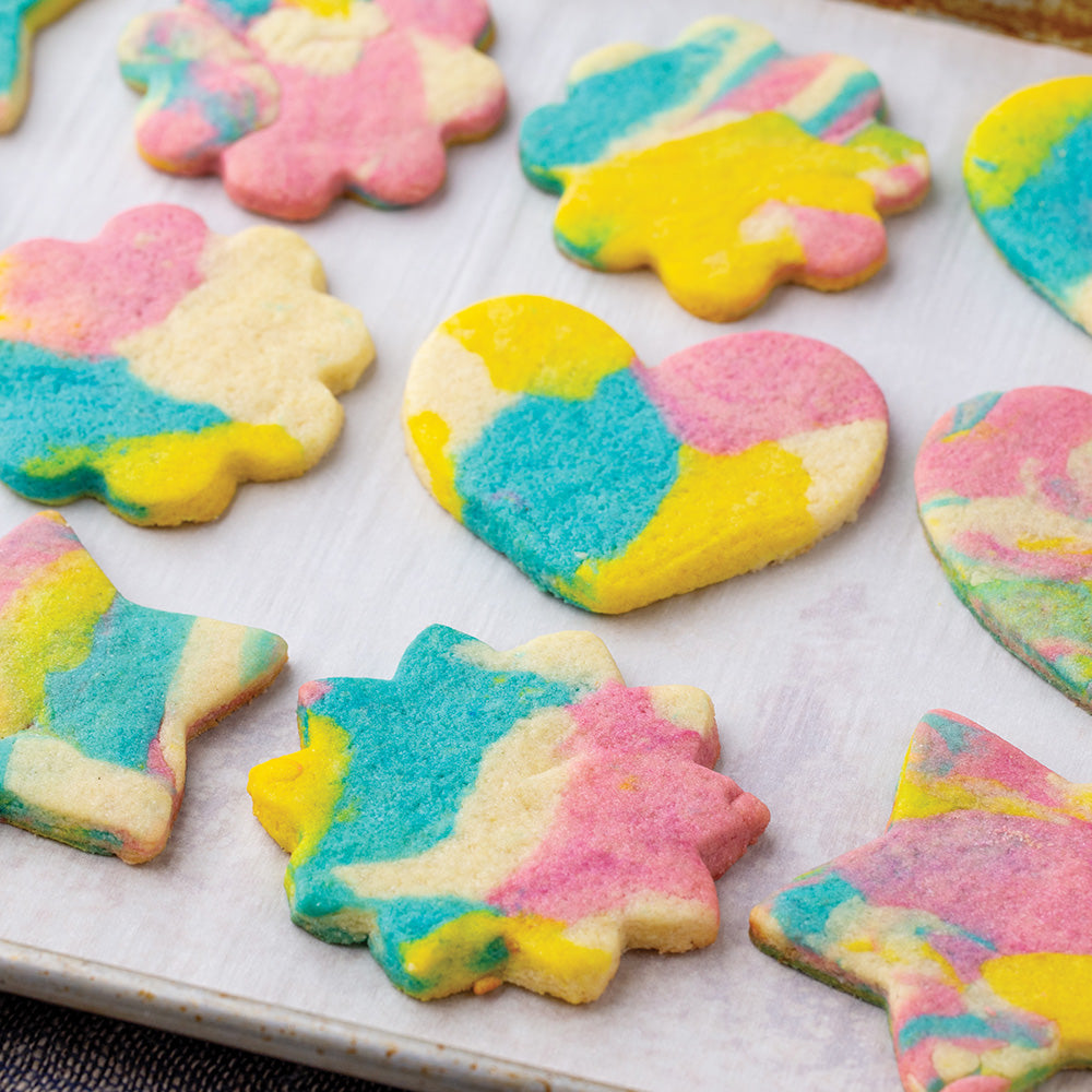 Sugar cookies made with dyed blue, yellow, and pink dough on a baking sheet